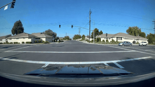 A video clip generated by Cosmos 3 for the autonomous driving domain. The video is from a vehicle’s point-of-view at an intersection. Another car crosses the intersection in front of this vehicle, and then the vehicle takes a left turn. The video looks realistic and shows houses, trees, and cars in the surroundings.